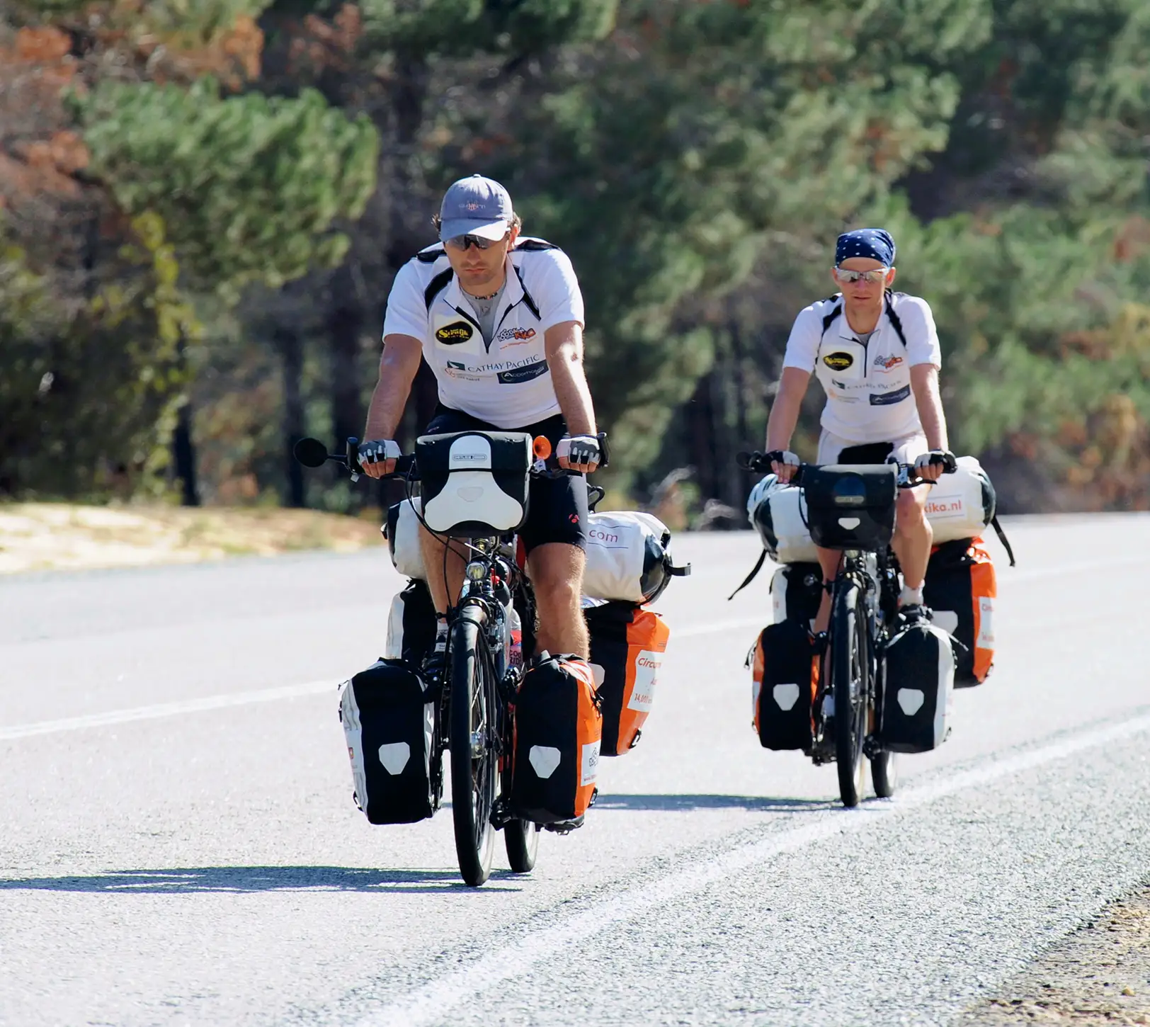 Two cyclists riding touring bikes with gear on an open road